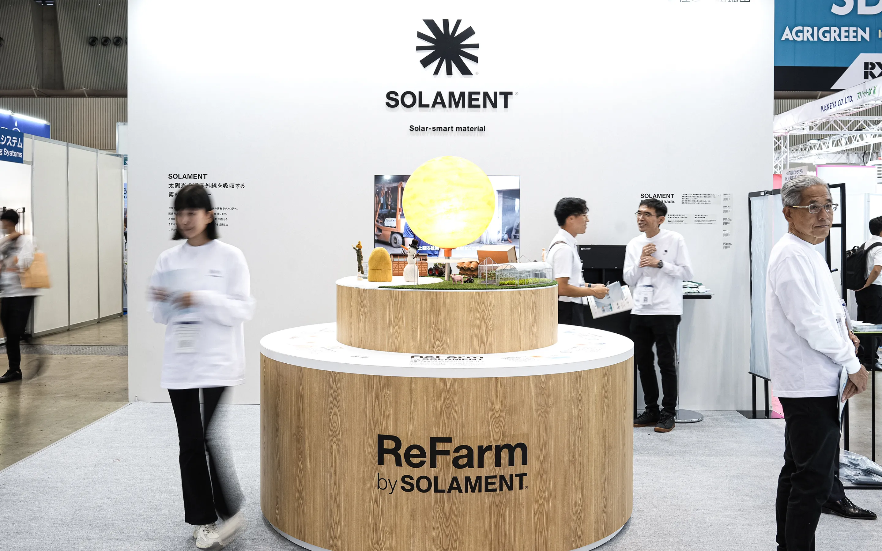 A visual from Agriculture WEEK. A central wood-grain display showcases ReFarm by SOLAMENT™, with a glowing sun, farm diorama, and surrounding visitors