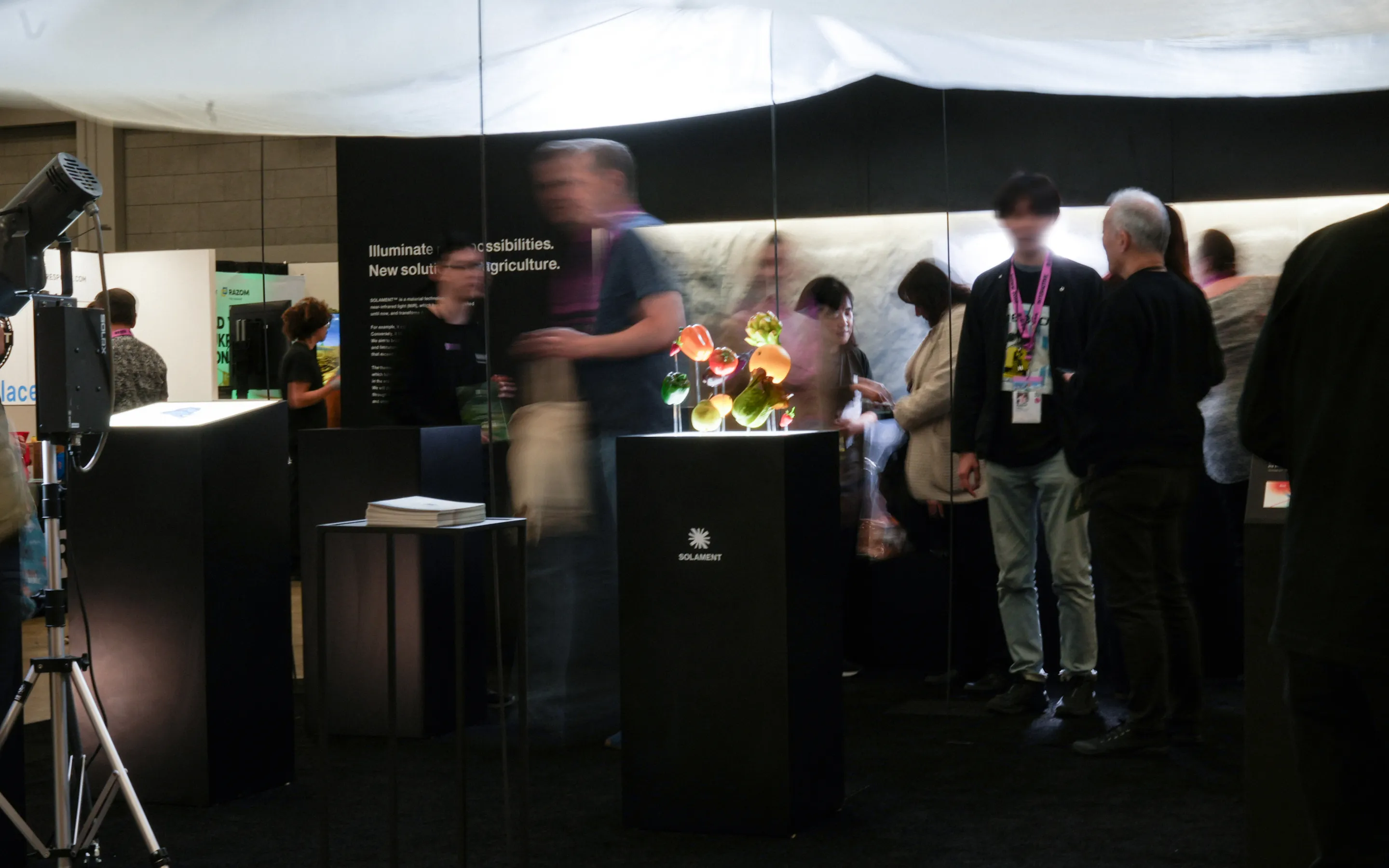 A visual from SXSW 2025. The SOLAMENT™ booth bustles with visitors admiring brightly lit colorful vegetables under a white shade