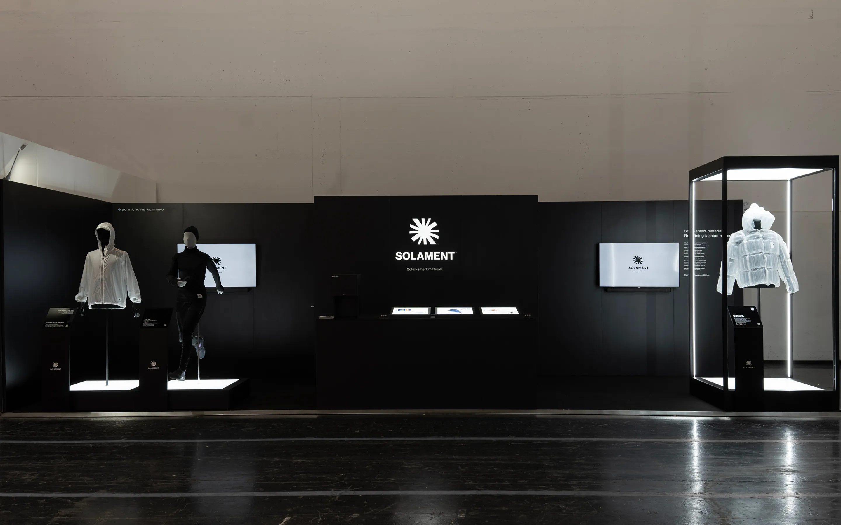 A visual of the SOLAMENT™ booth at ISPO, featuring a black‑toned space with a large brand logo and illuminated mannequins dressed in concept models