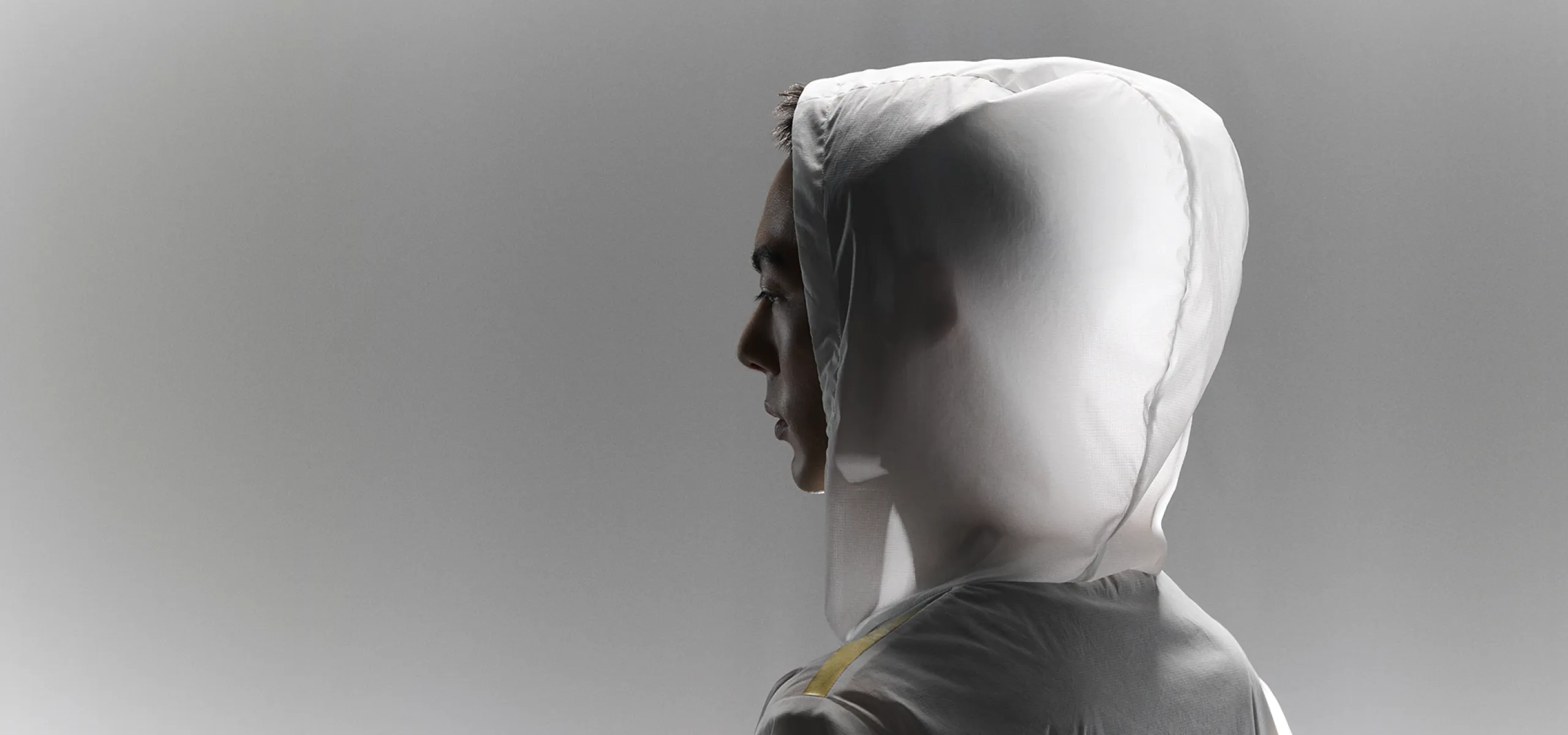 A close-up visual of a person wearing the lightweight, semi‑transparent white hooded CROSS‑DOOR JACKET, facing left with the hood up