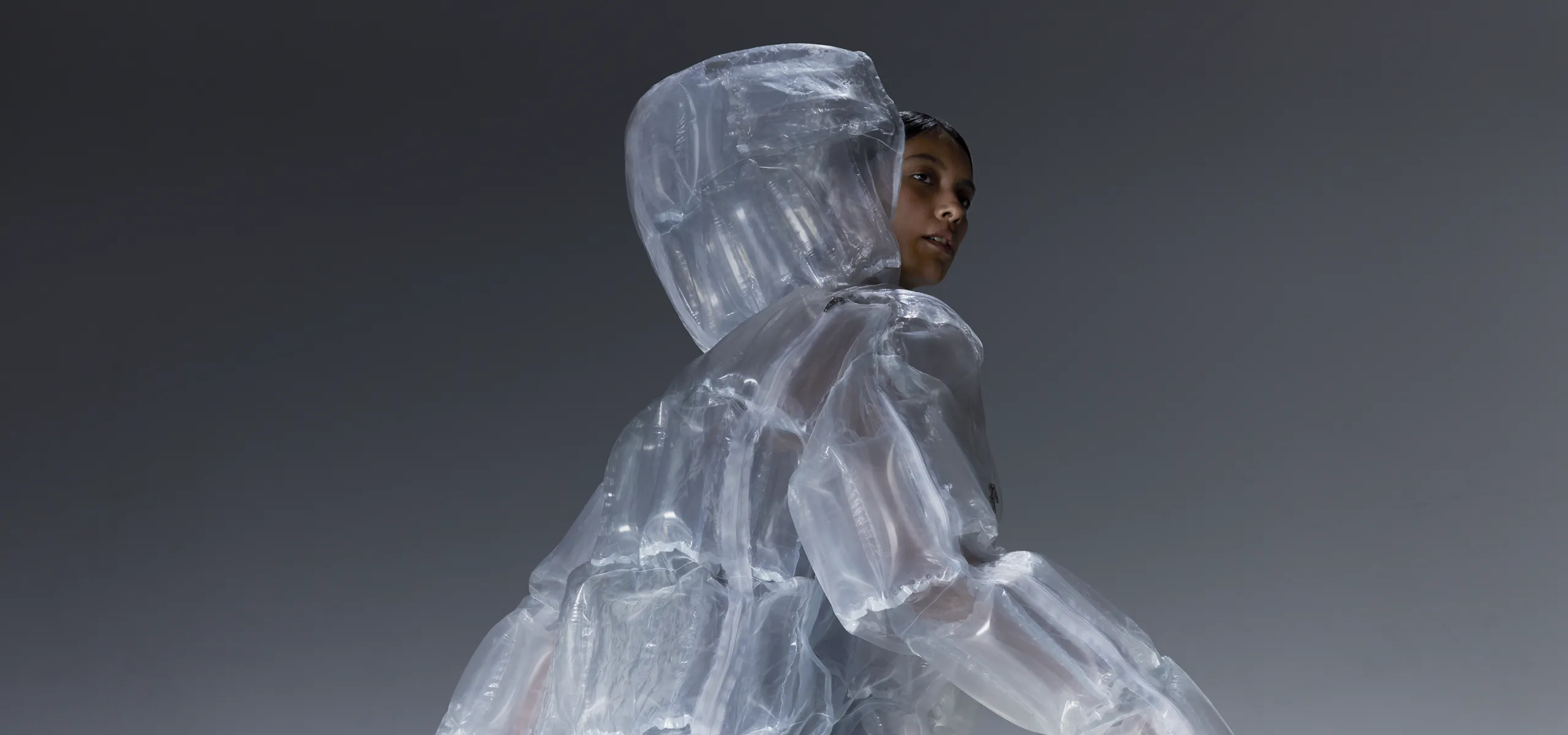 A visual of a person wearing the DOWN-LESS DOWN JACKET, a down‑free jacket made with the innovative transparent material, looking back over their shoulder