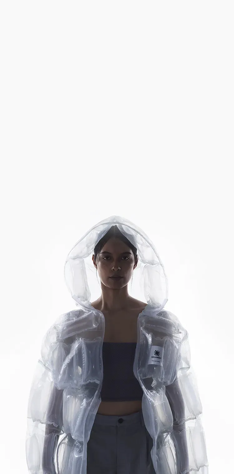 Woman wearing a transparent hooded jacket, DOWN-LESS DOWN JACKET, expressing high functionality through an air-filled structure using minimal resources.