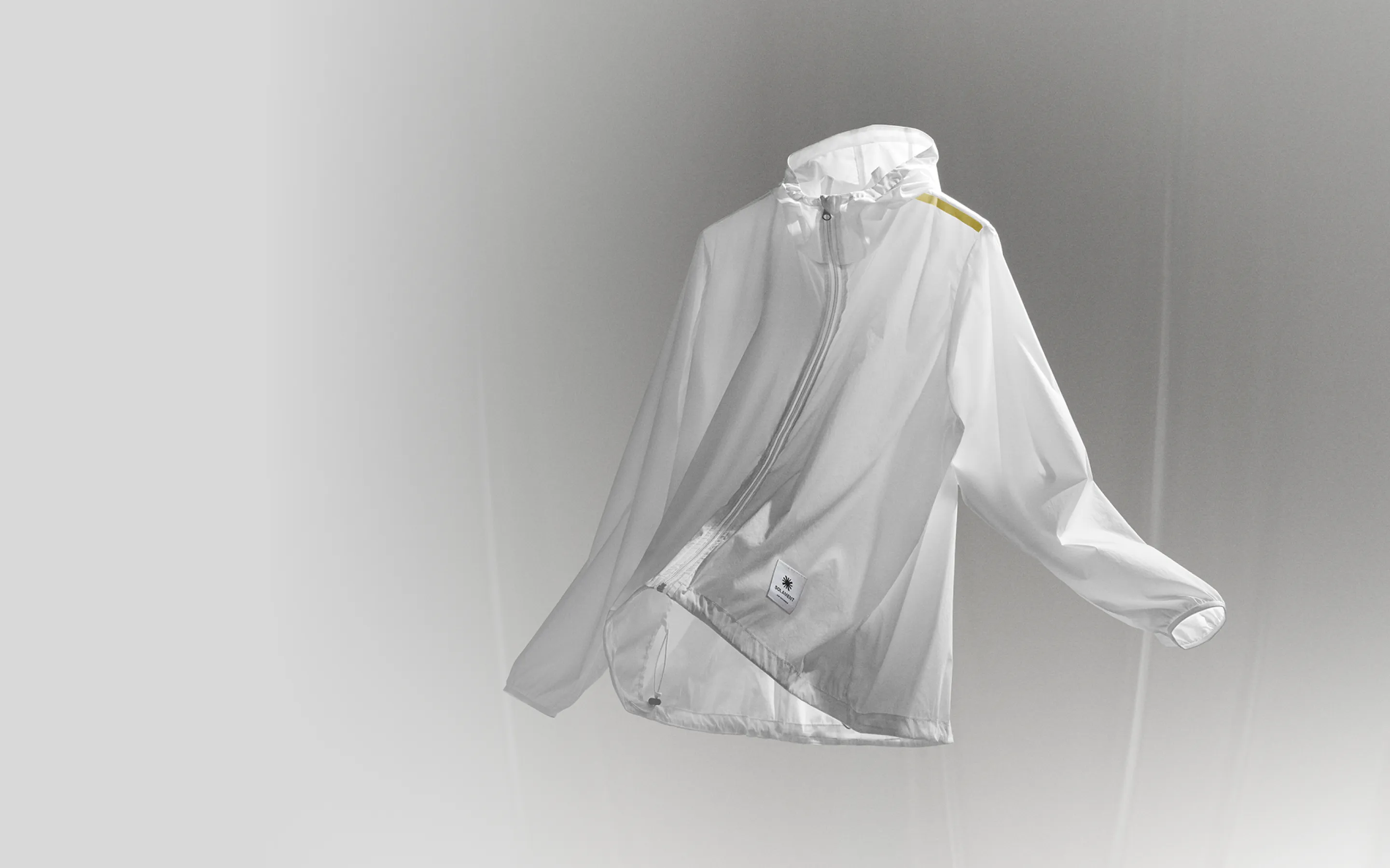 White semi‑transparent hooded parka floating in the air, featuring a yellow reflector and a SOLAMENT™ logo tag, expressing unconventional warmth.