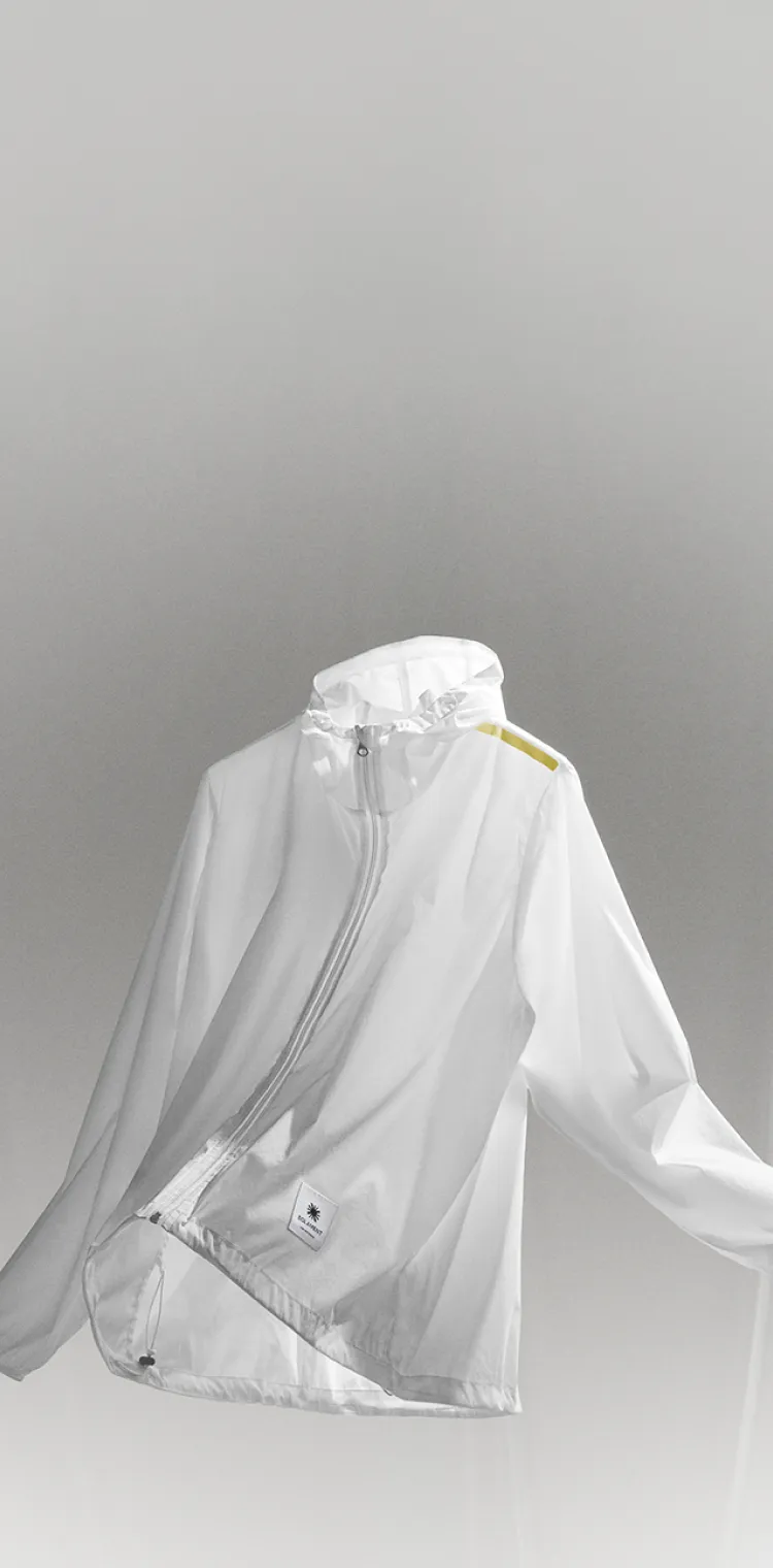 White semi‑transparent hooded parka floating in the air, featuring a yellow reflector and a SOLAMENT™ logo tag, expressing unconventional warmth.