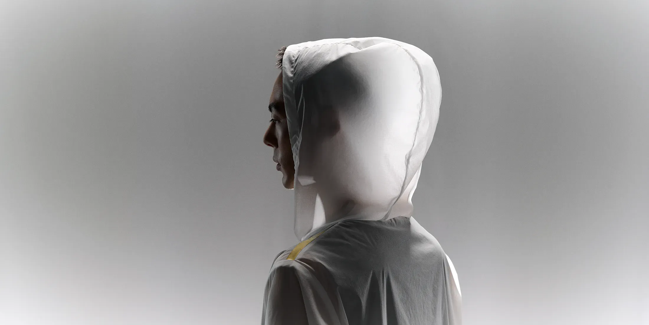 Side profile of a man in the CROSS-DOOR JACKET hood, highlighting the thin, lightweight fabric translucent in the light.
