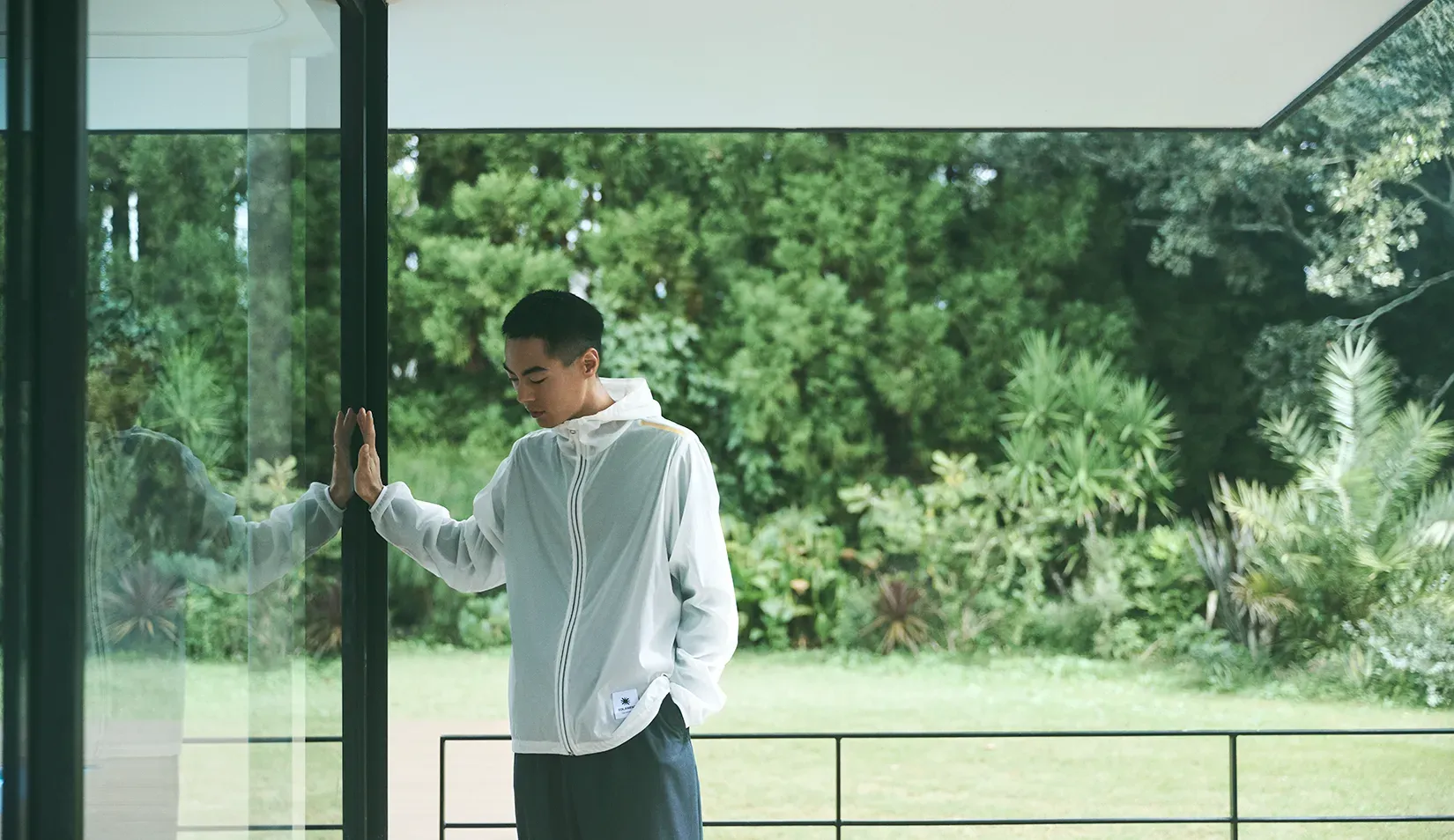 Man by a window with a green garden behind him, wearing the CROSS-DOOR JACKET for both indoor and everyday use.