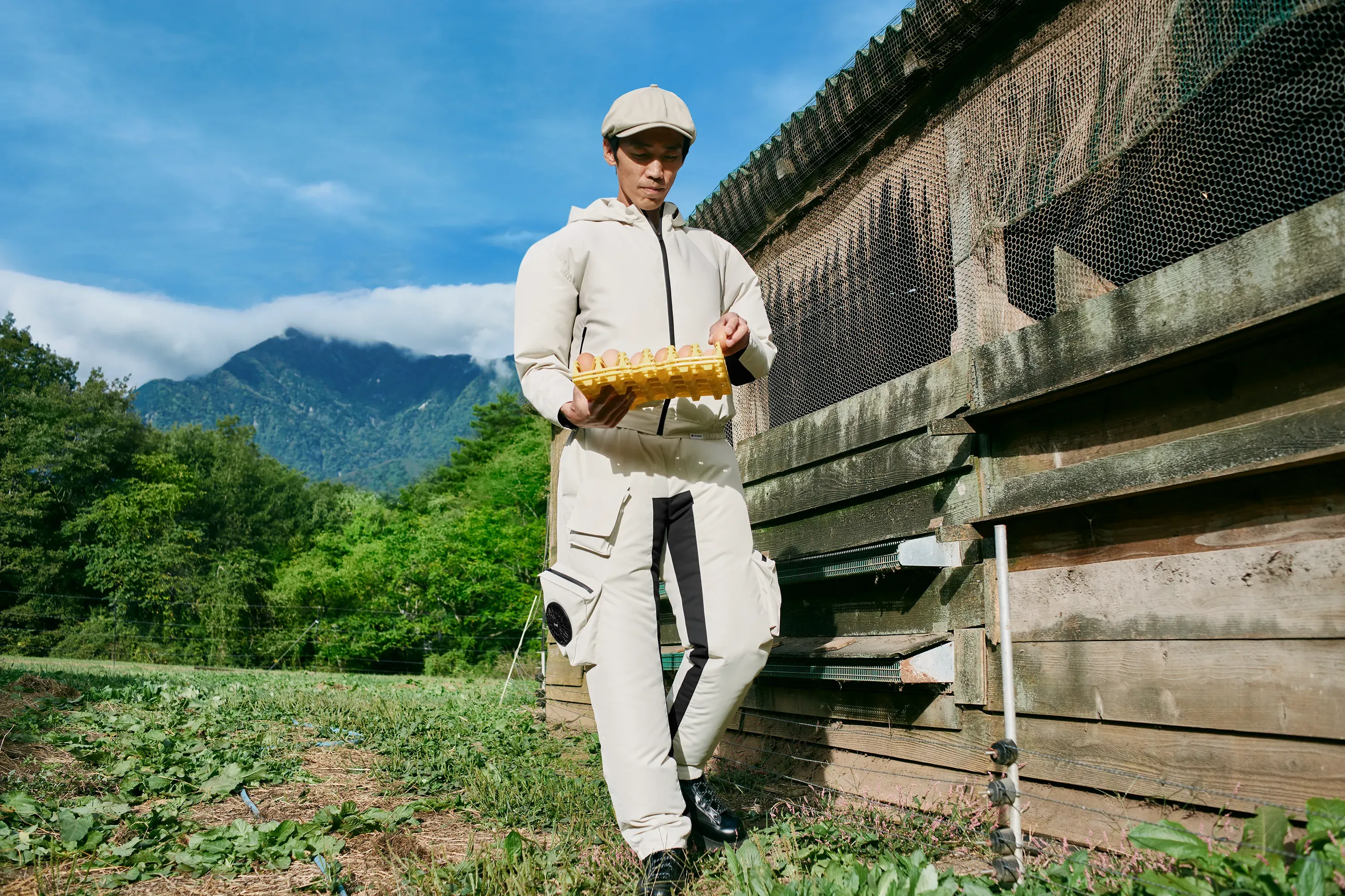 A full-body view of a man holding an egg tray, wearing off-white "HOPE WEAR for Farm Type A" with KUCHOFUKU fans at waist and thighs.