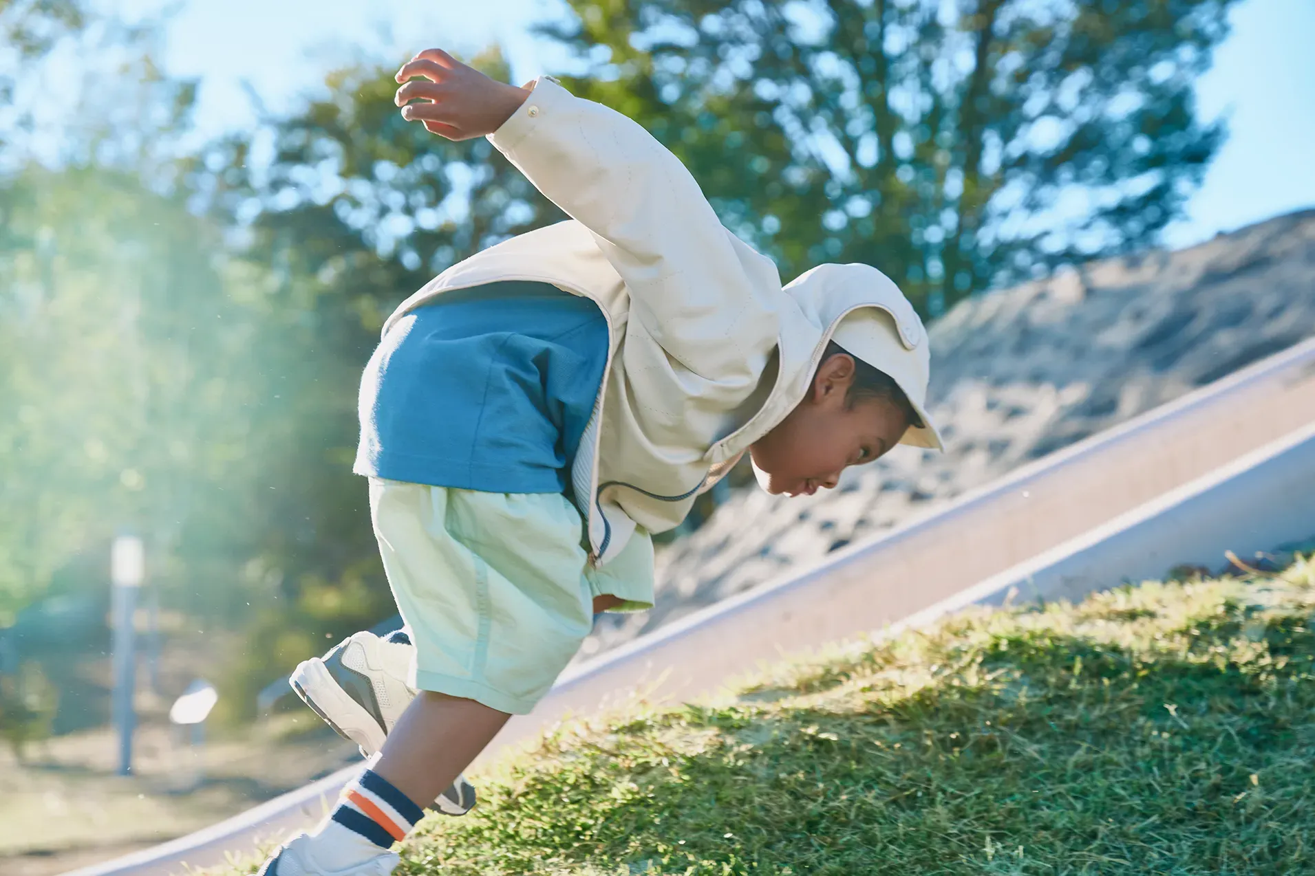 Boy playing outdoors in a pleated jacket, HOPE WEAR for Play, the pleats billowing in the wind.