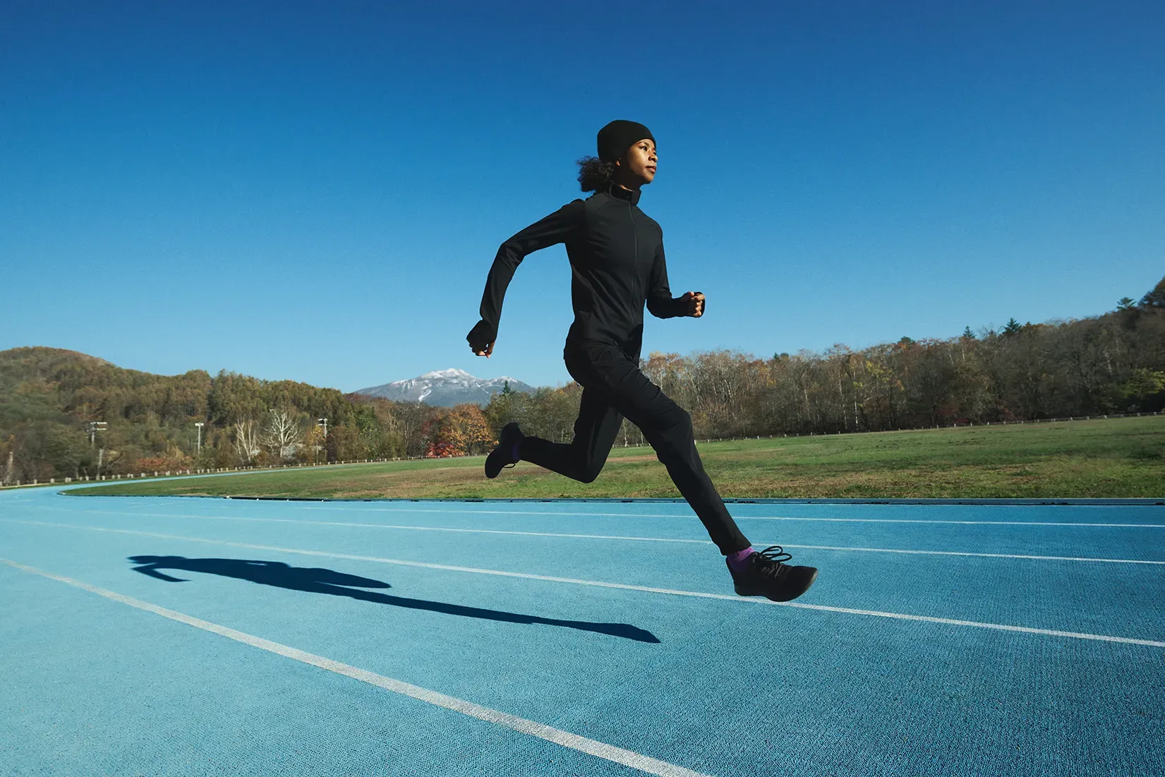 Woman running fast on a track overlooking mountains, wearing SOLAR-PERFORMANCE WEAR to show maintained performance in cold conditions.