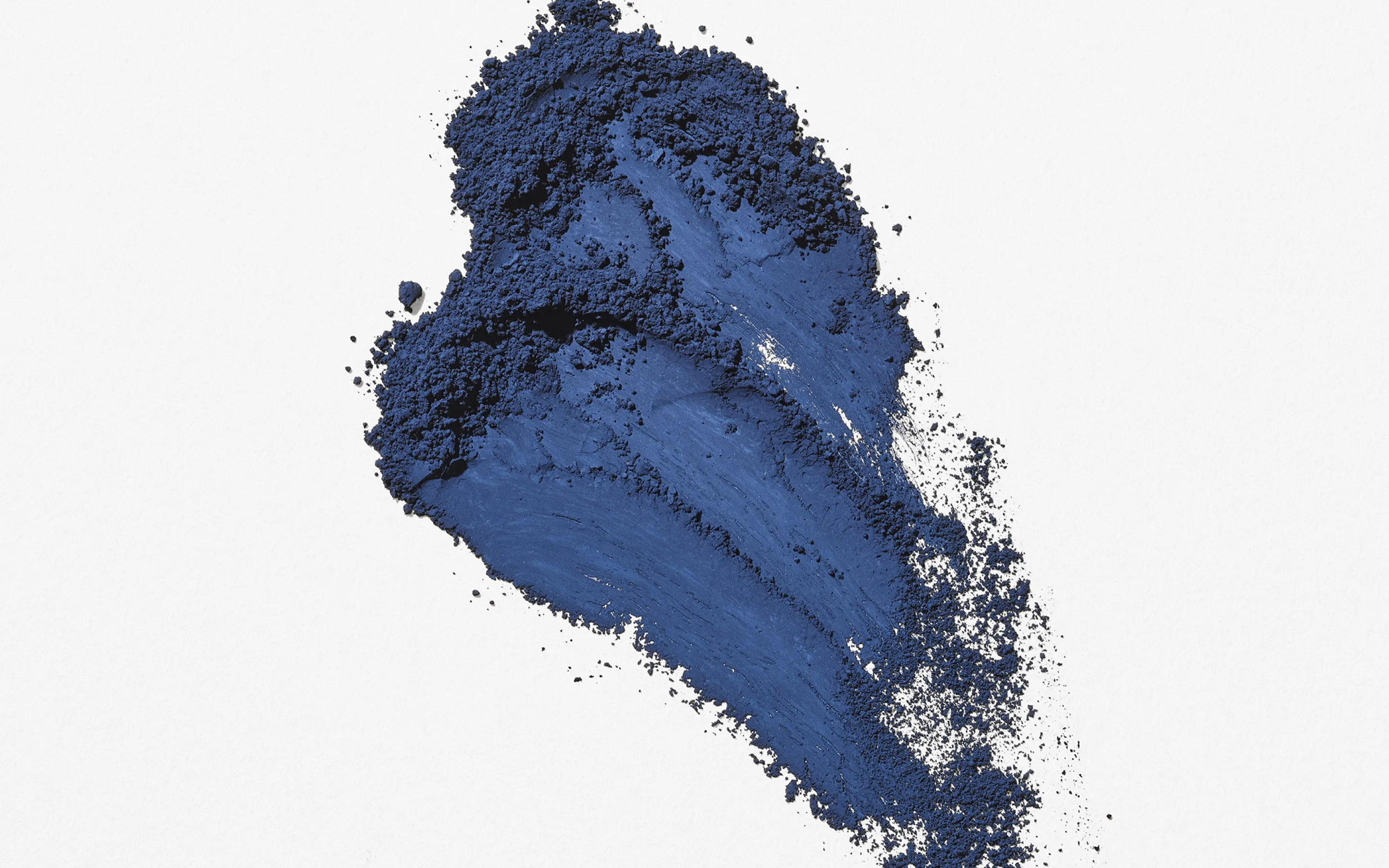 A visual of deep navy-blue micro particles spreading across a white background with a textured, brush-painted appearance